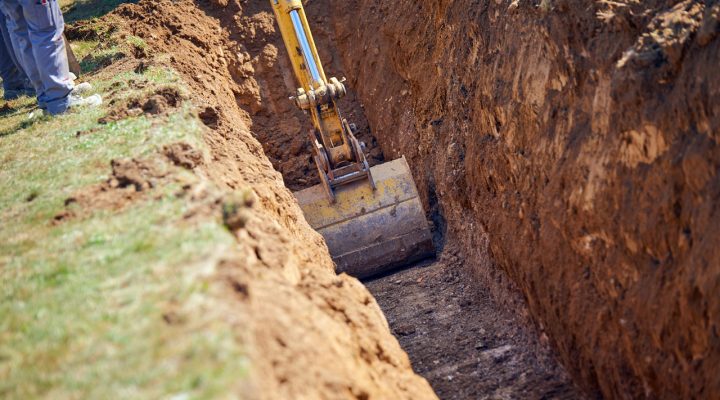 Professional Ditch Excavation Service by Rooney Excavating Yellow excavator digging a precise trench in a grassy field for utility or drainage installation.