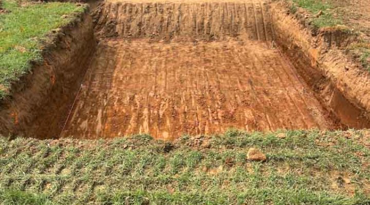 Precise Foundation Trenching for a New Custom Home A deep, rectangular excavation for a home’s foundation, with clean, straight walls and tire tracks on the compacted soil, located in front of a modern brick house.