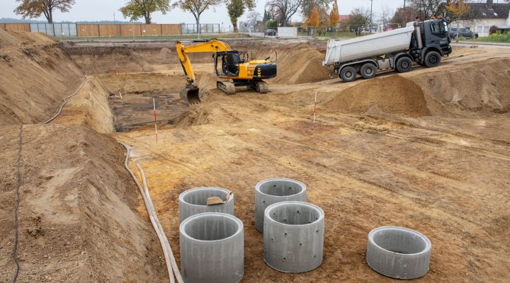 Rooney Excavating Site in Maryville: Foundation Work and Material Hauling Wide shot of a construction site featuring an excavator, a dump truck, and precast concrete rings ready for installation.