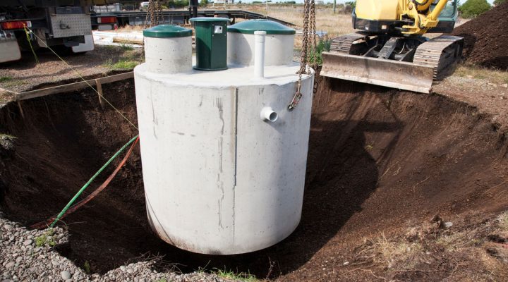 Installation of a Concrete Septic Tank by Rooney Excavating A large concrete septic tank being carefully lowered into a prepared excavation pit with an excavator nearby.