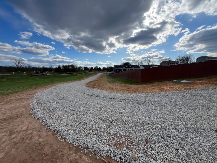 Freshly installed gravel driveway curving across a graded lot beside a fenced yard: driveway and foundation excavation by Rooney Excavating of Seymour, TN