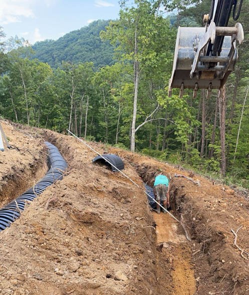 Worker in a hillside trench beside corrugated drain pipe, seen from the excavator: excavation by Rooney Excavating of Seymour, TN