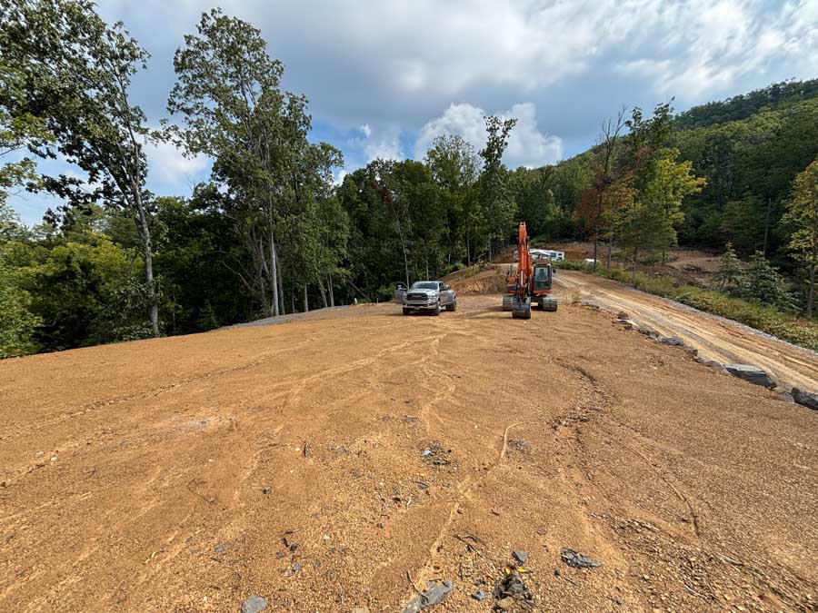 Large graded pad with an excavator and pickup truck at the edge of a wooded site: site preparation by Rooney Excavating of Seymour, TN