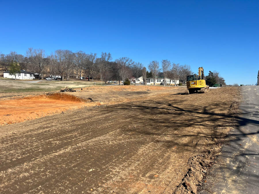Excavator on freshly graded ground beside a paved road: site preparation by Rooney Excavating of Seymour, TN