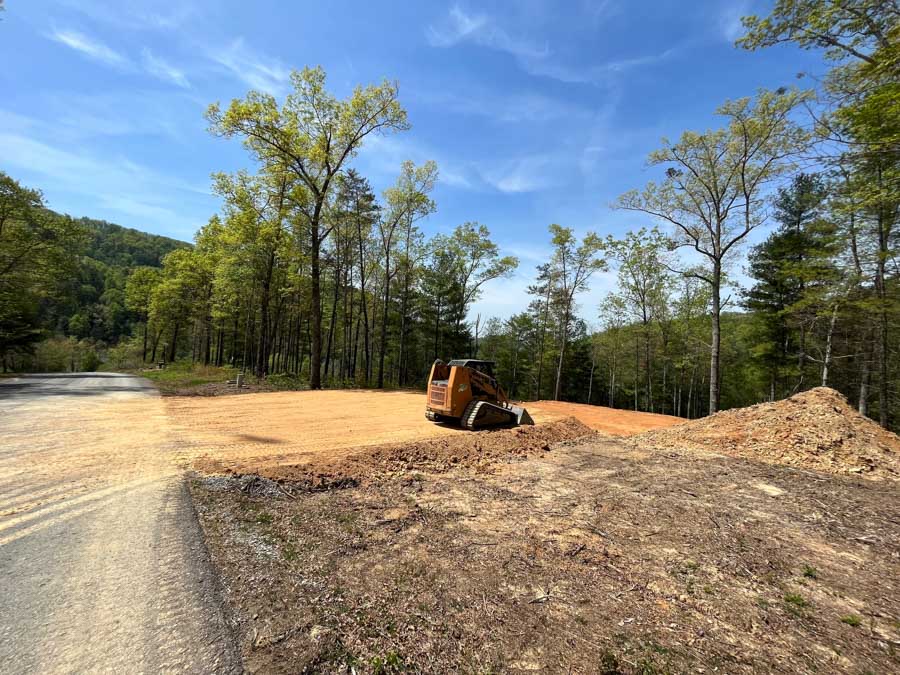 Compact track loader leveling soil on a wooded building site beside a gravel road: excavation by Rooney Excavating of Seymour, TN